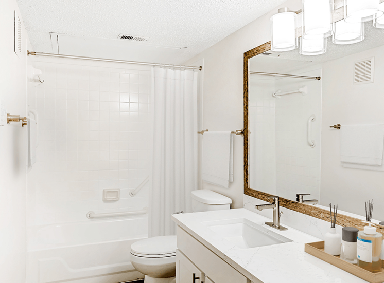 Virtually staged bathroom with white quartz countertop, white cabinetry, large mirror and white shower curtain